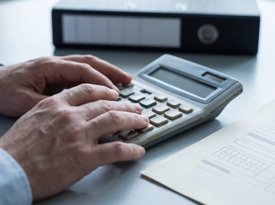 Hands totalling a purchase order on a desk calculator